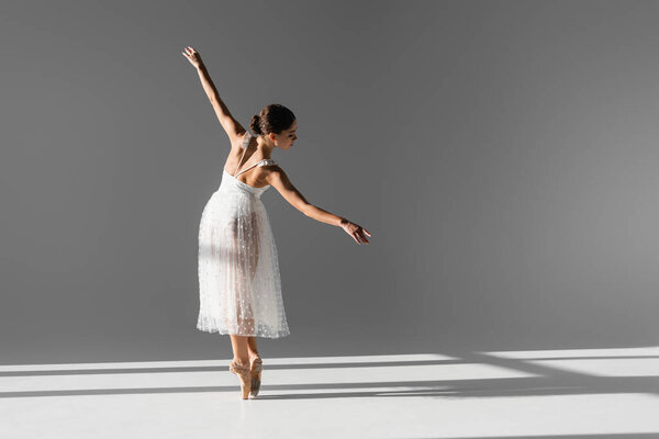 Side view of elegant ballerina in pointe shoes on grey background with sunlight