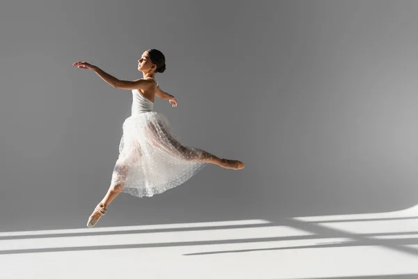 Zijaanzicht Van Professionele Ballerina Springen Grijze Achtergrond Met Zonlicht — Stockfoto