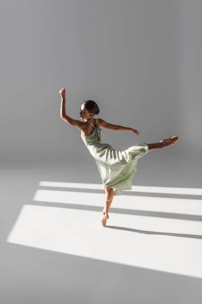 Балерина Танцует Стоит Одной Ноге Сером Фоне Солнечным Светом — стоковое фото
