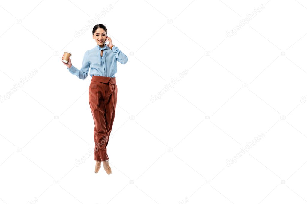 Smiling ballerina talking on mobile phone and holding paper cup isolated on white 