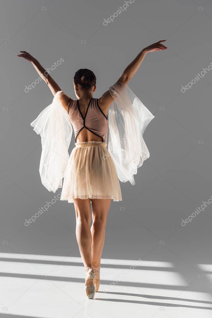 Back view of ballerina dancing with cloth on grey background with sunlight