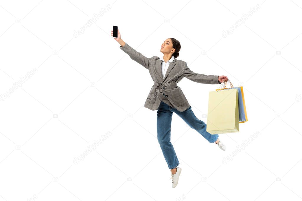 Ballerina with shopping bags holding cellphone while jumping isolated on white 