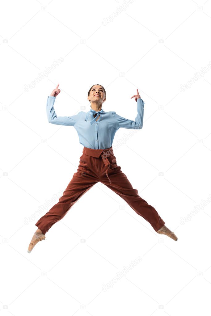 Smiling ballerina pointing with fingers while jumping isolated on white 