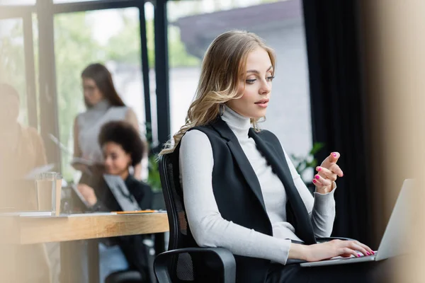 Blonde Businesswoman Pointing Laptop While Working Office Blurred Multiethnic Colleagues — Stock Photo, Image