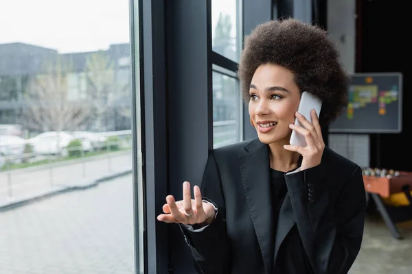 Mulher Negócios Afro Americana Gesticulando Enquanto Falava Smartphone Perto Janela — Fotografia de Stock