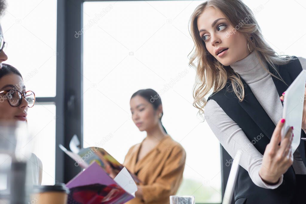 blonde businesswoman showing digital tablet to colleague in eyeglasses
