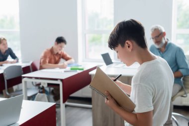 Not defteri olan Asyalı okul çocuğu sınıfta duruyor. 