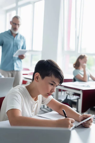 Asian Schoolboy Holding Smartphone Writing Notebook Classroom — Stock Photo, Image