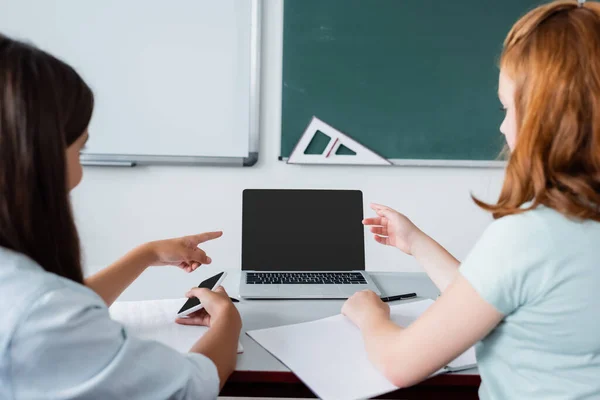 Blurred schoolgirls pointing at laptop during lesson in school