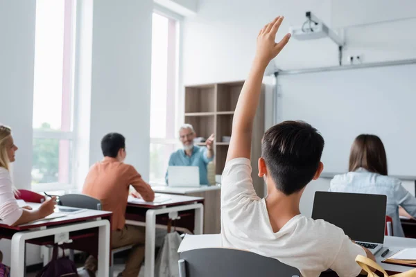 Alumno Levantando Mano Cerca Computadora Portátil Compañeros Clase Borrosos —  Fotos de Stock