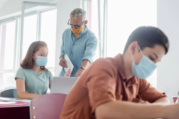 Maestra Madura Máscara Médica Pie Cerca Colegiala Apuntando Computadora Portátil —  Fotos de Stock