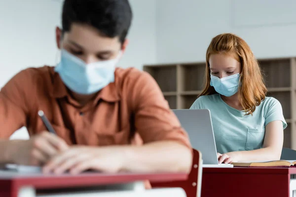 Iskolásfiú Orvosi Maszk Segítségével Laptop Közelében Elmosódott Osztálytárs — Stock Fotó