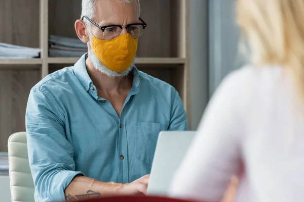 Mature teacher in protective mask using laptop during lesson