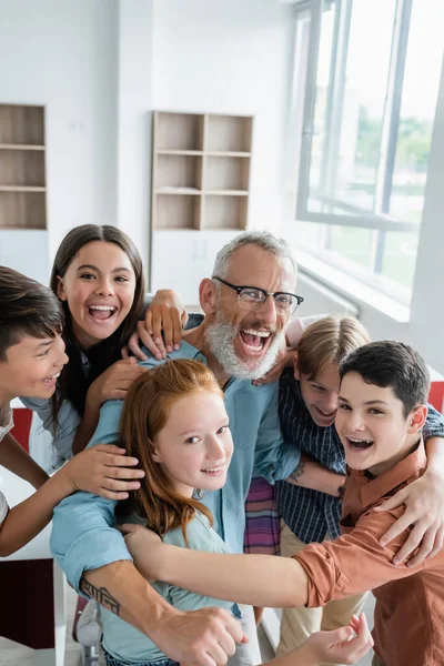 Vrolijke Multiculturele Tieners Omarmen Lachende Leraar Kijken Naar Camera Klas — Stockfoto