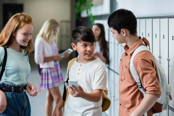 Asiatisk Pojke Ler Medan Håller Smartphone Nära Vänner Skolan Korridor — Stockfoto