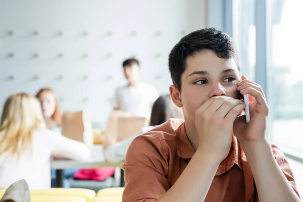 Teenage Boy Gossiping Smartphone School Eatery Classmates Blurred Background — Stock Photo, Image