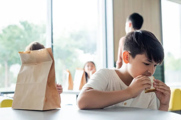 Азиатский Школьник Ест Сэндвич Одиночестве Столовой Рядом Размытыми Подростками — стоковое фото