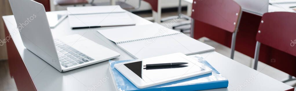 digital tablet and laptop near notebooks on desk in modern school, banner