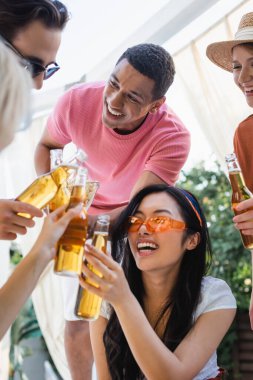 Neşeli çok kültürlü arkadaşlar yaz partisinde bira şişeleriyle tıkırdıyorlar.