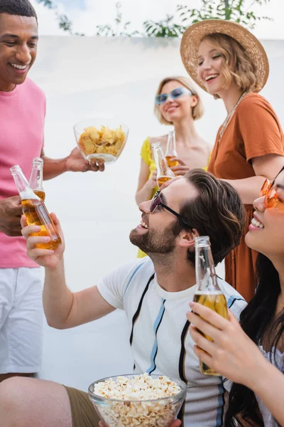 Happy Interracial Men Clinking Bottles Beer Smiling Women — Zdjęcie stockowe