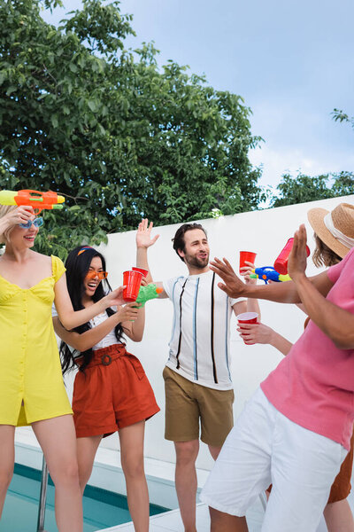 happy interracial friends having fun with water pistols during summer party