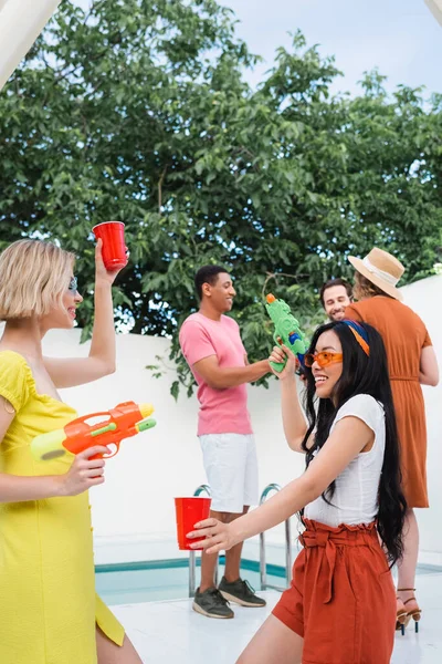 Mujeres Interracial Jugando Con Pistolas Agua Cerca Amigos Multiétnicos Sobre — Foto de Stock