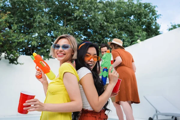 Fröhliche Interrassische Frauen Mit Wasserpistolen Die Rücken Rücken Bei Einer — Stockfoto