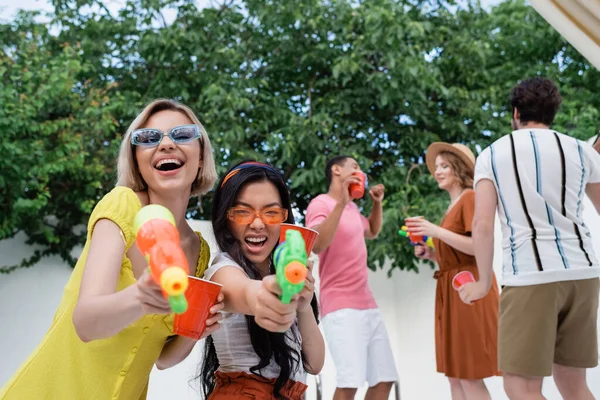 Excited Interracial Women Water Pistols Laughing Camera Blurred Friends — Stockfoto