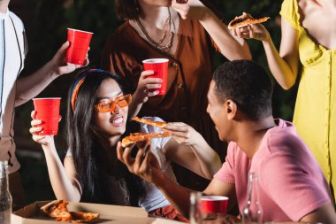 Plastik bardaklar ve açık havada pizza tutan mutlu çok kültürlü arkadaşlar. 