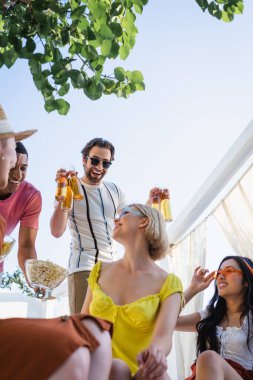 Verandada çok ırklı dostların yanında bira içen bir adamın düşük açılı görüntüsü 