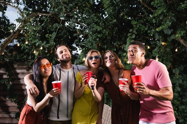 Amigos Multiétnicos Alegres Segurando Copos Plástico Enquanto Cantava Karaoke Jardim — Fotografia de Stock