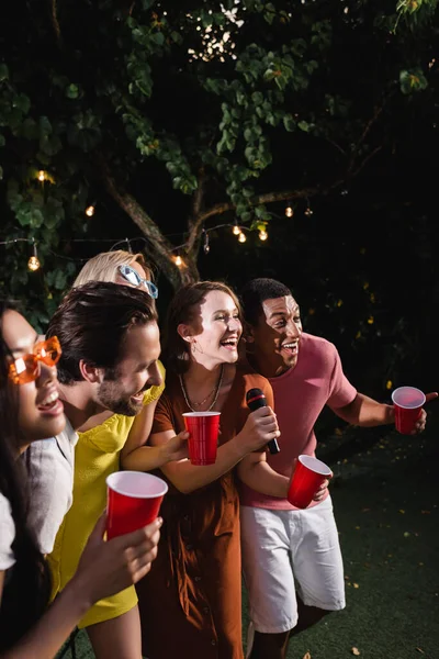 Sonriendo Jóvenes Interracial Cantando Karaoke Sosteniendo Vasos Plástico Aire Libre — Foto de Stock