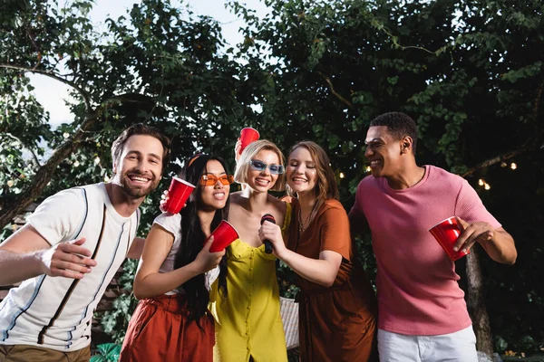 Mulheres Multiétnicas Cantando Karaoke Perto Amigos Com Copos Plástico — Fotografia de Stock