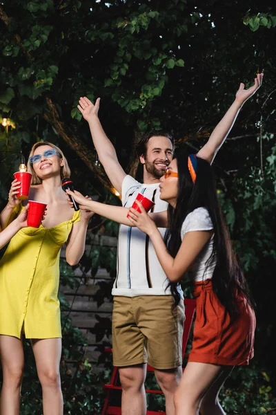 stock image Cheerful man standing near asian friend with microphone and plastic cup outdoors 