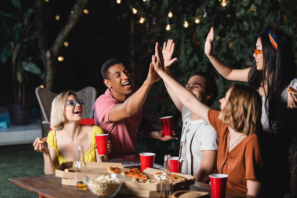 Молодые мультикультурные друзья дают пять на улице возле пива и пиццы 