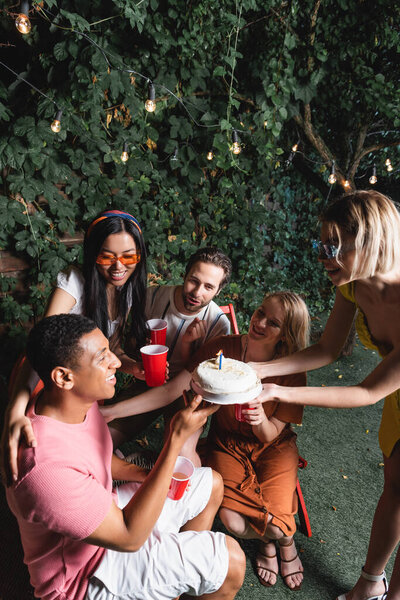 Cheerful interracial friends with plastic cups celebrating birthday of african american man outdoors 