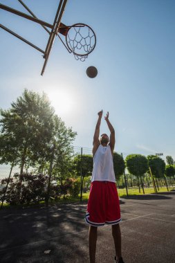 Wide angle view of african american player throwing ball in basketball hoop outdoors  clipart