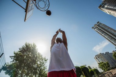 Bottom view of african american man throwing ball in basketball hoop outdoors  clipart