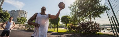Neşeli bir adam basketbol topunu açık hava oyun alanında arkadaşının yanında tutuyor. 