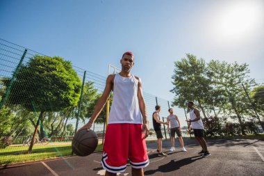 Basketbol toplu Afro-Amerikan bir adamın oyun parkındaki arkadaşlarının yakınındaki kameraya bakış açısı düşük. 