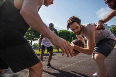 Genç adam basketbol topunu çok ırklı oyuncuların yanında tutuyor. 