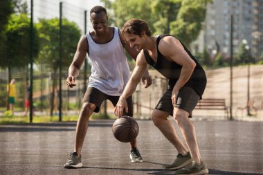 Dışarıda basketbol oynayan gülümseyen ırklar arası adamlar. 