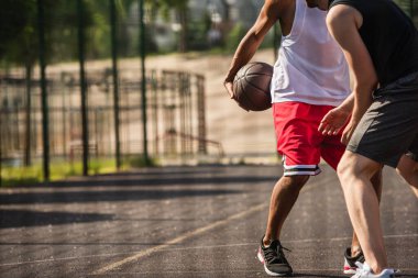 Açık havada arkadaşının yanında basketbol topu tutan Afro-Amerikan sporcunun görüntüsü. 