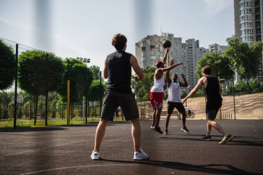 Çocuk parkında basketbol oynarken atlayan çok ırklı genç sporcular 