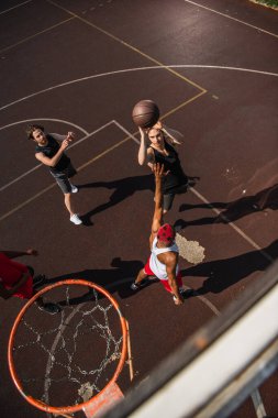 Overhead view of man with basketball ball jumping near interracial friends and hoop outdoors  clipart