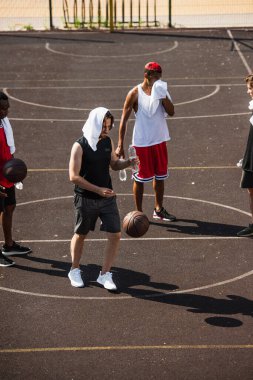 Young man with towel and water standing near basketball ball and multiethnic friends  clipart