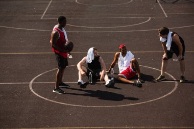 Gülen çoklu etnik kökenli sporcular basketbol topu ve su şişeleriyle oyun alanında konuşuyorlar. 