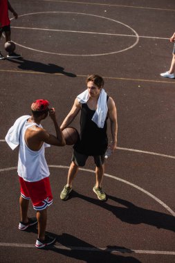 Basketbol topu ve su taşıyan bir adamın oyun parkındaki Afrikalı Amerikalı arkadaşının yanında durduğu yüksek açı. 