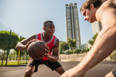 Konsantre olmuş Afrikalı Amerikalı oyuncu, yarışma sırasında arkadaşının yanında basketbol topu tutuyor. 