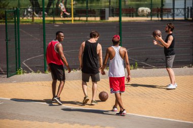 Basketbol topları olan neşeli çoklu etnik arkadaşlar dışarıda oyun sahasının yanında yürüyorlar. 